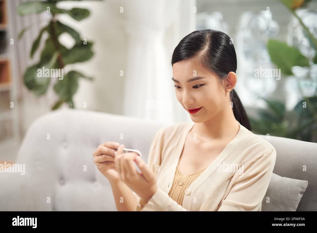 Sorridente attraente donna asiatica guardando le sue unghie perfette dopo archiviarli Foto Stock