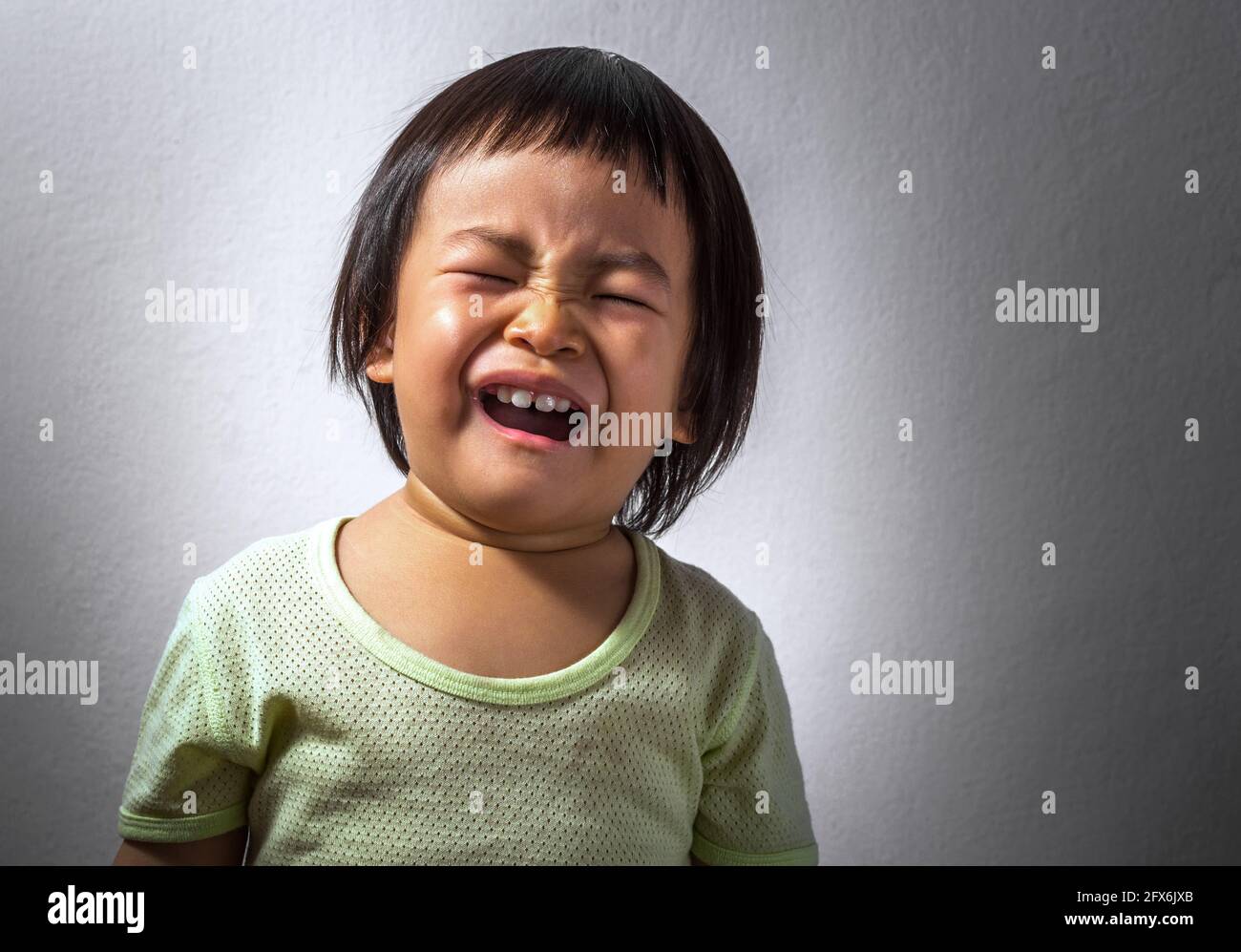 Ritratto di una bambina asiatica sconvolto, piangendo da sola, lo sfondo di una parete bianca scura, spazio vuoto per il testo. Foto Stock