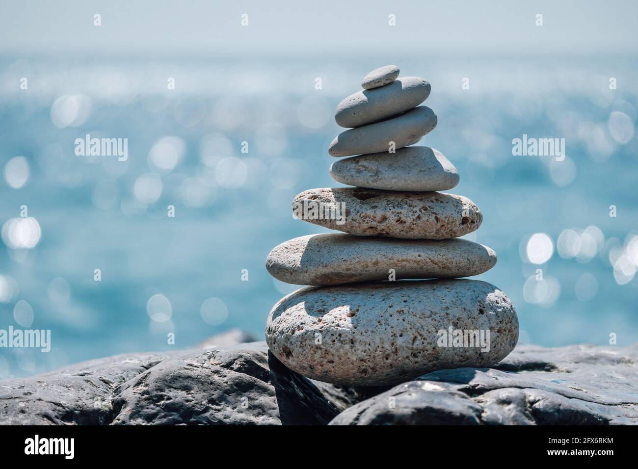 Equilibrata piramide di ciottoli sulla spiaggia in una giornata di sole. Abstract Sea bokeh sullo sfondo. Messa a fuoco selettiva. Pietre Zen sulla spiaggia di mare, meditazione Foto Stock