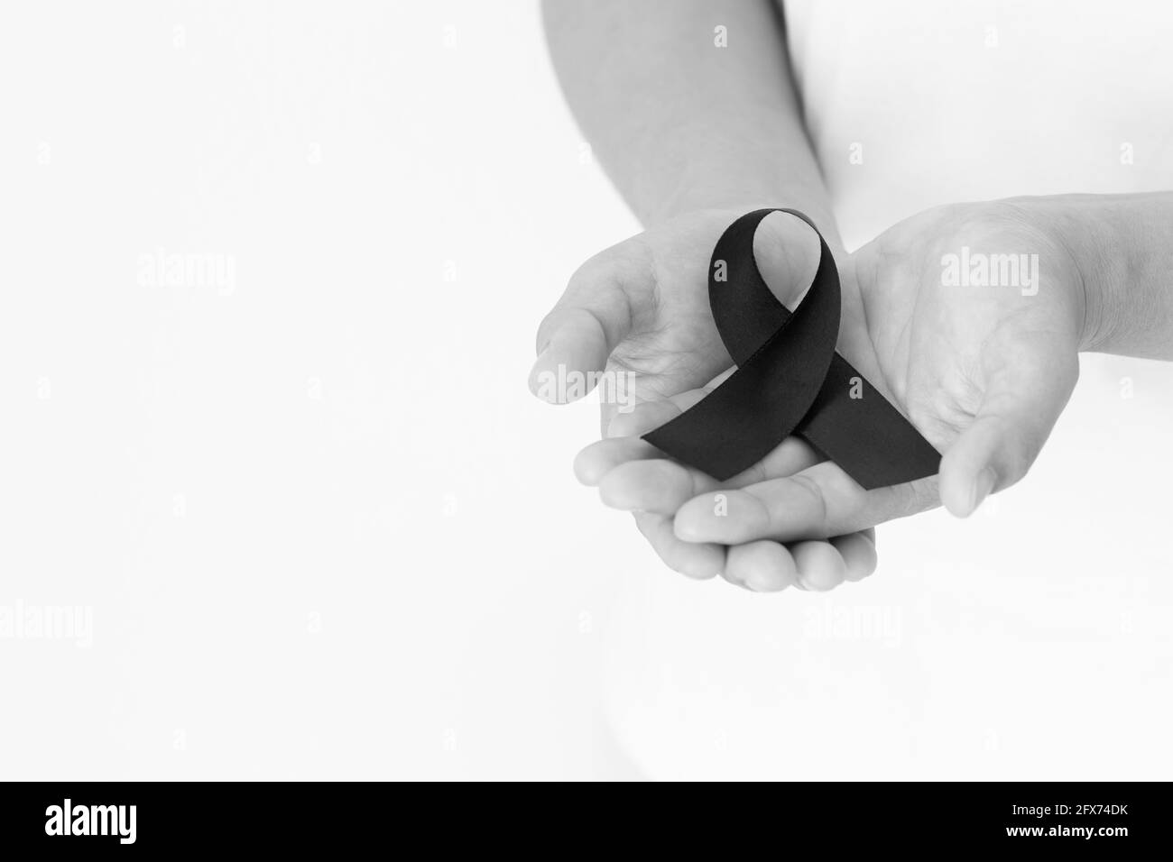 Mano che tiene nastro nero su sfondo bianco con spazio di copia, simbolo del mese di consapevolezza del cancro della pelle il mese di maggio, cancro del melanoma, nastro di lutto simbolico Foto Stock