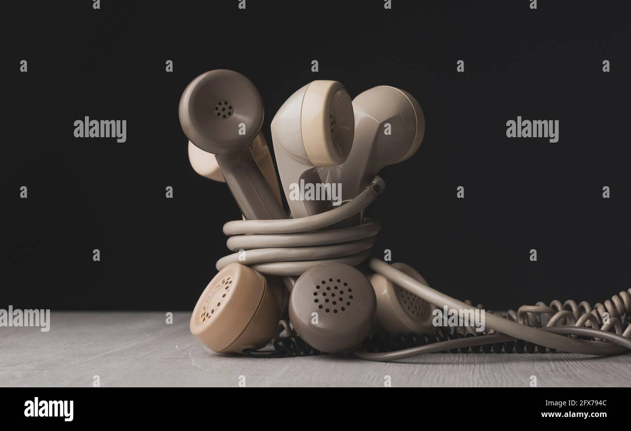 Vecchi ricevitori telefonici legati insieme su una scrivania, concetto di linee telefoniche inceppate Foto Stock