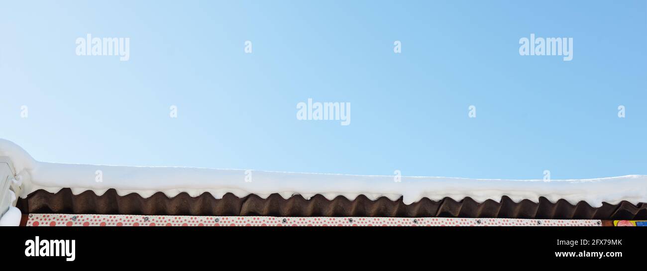 Un tetto innevato di una casa di legno. Edificio in legno con molta neve sul tetto Foto Stock