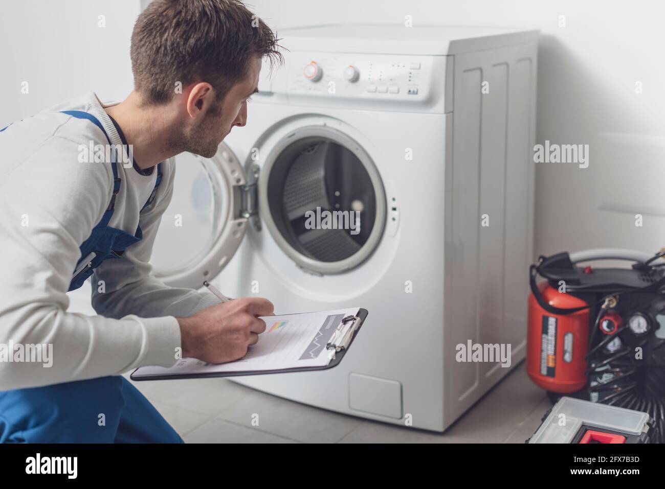 Tecnico professionale che controlla una lavatrice, sta scrivendo su una clipboard Foto Stock