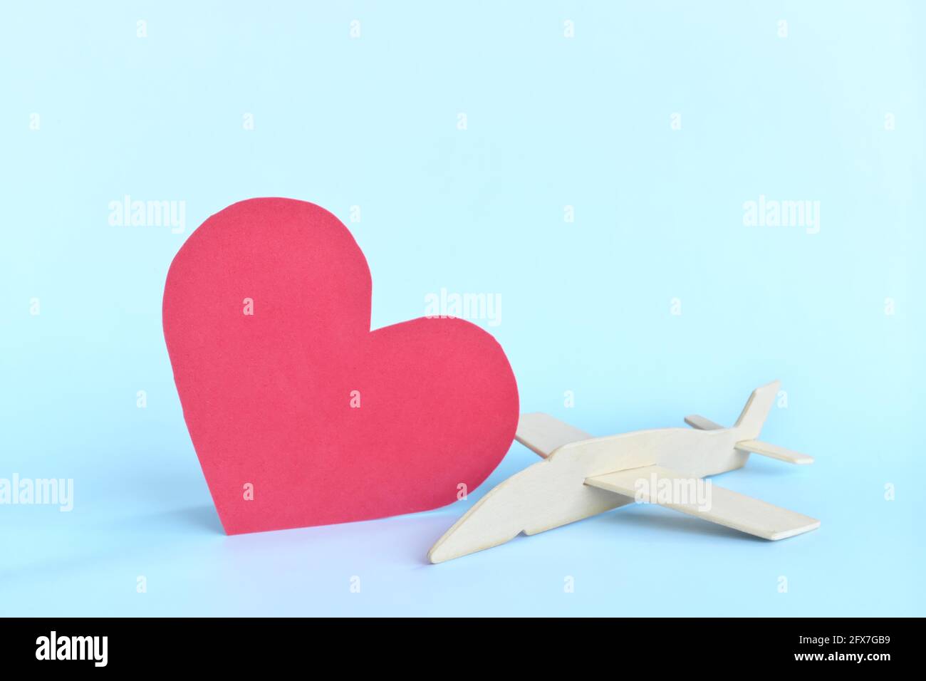 Modello di aeroplano in legno accanto a una forma a cuore rosso su sfondo blu cielo. Amore viaggio e vacanza concetto. Foto Stock