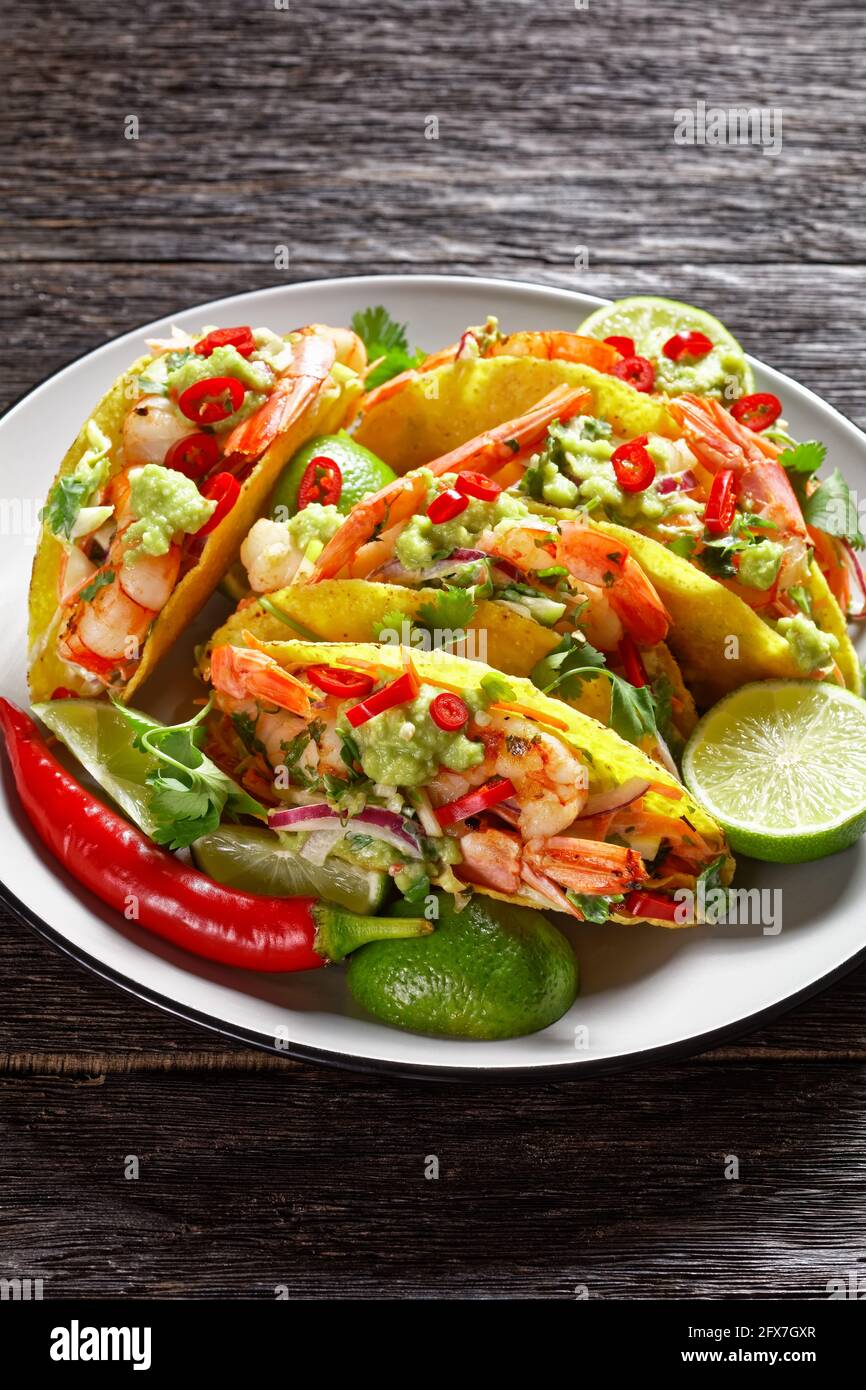 conchiglie di taco con gamberi alla griglia, insalata di cavolo, lime e guacamole su un piatto su un tavolo di legno Foto Stock