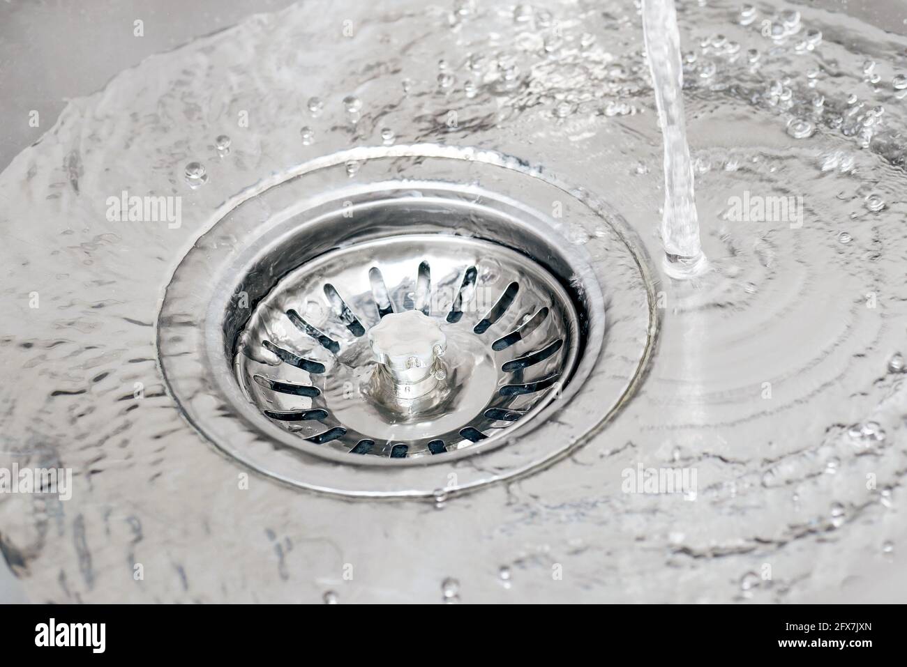 Acqua che scorre dal rubinetto in un lavello e che versa nello scarico con il tappo del filtro a rete. Foto Stock