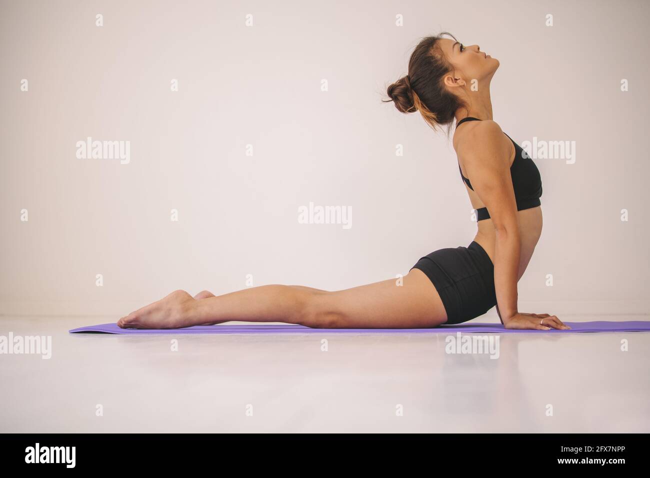 Vista laterale della donna che fa stretch core sul tappetino fitness. Giovane donna in abbigliamento sportivo che pratica Cobra posa yoga asana in palestra. Foto Stock