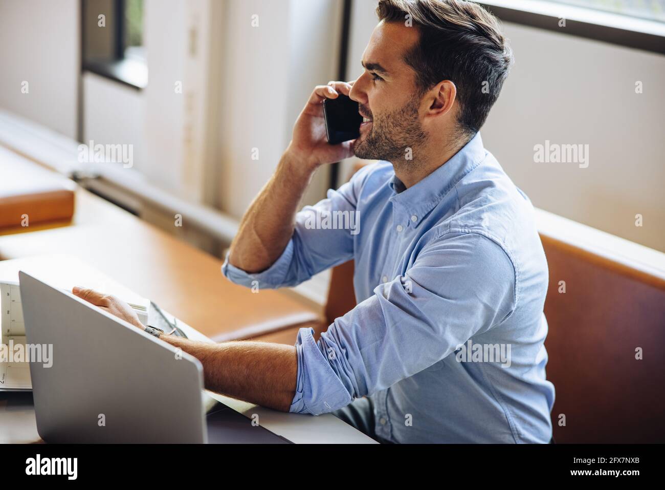 Uomo che parla al telefono cellulare alla scrivania in ufficio. uomo d'affari seduto alla scrivania e che parla con uno smartphone. Foto Stock