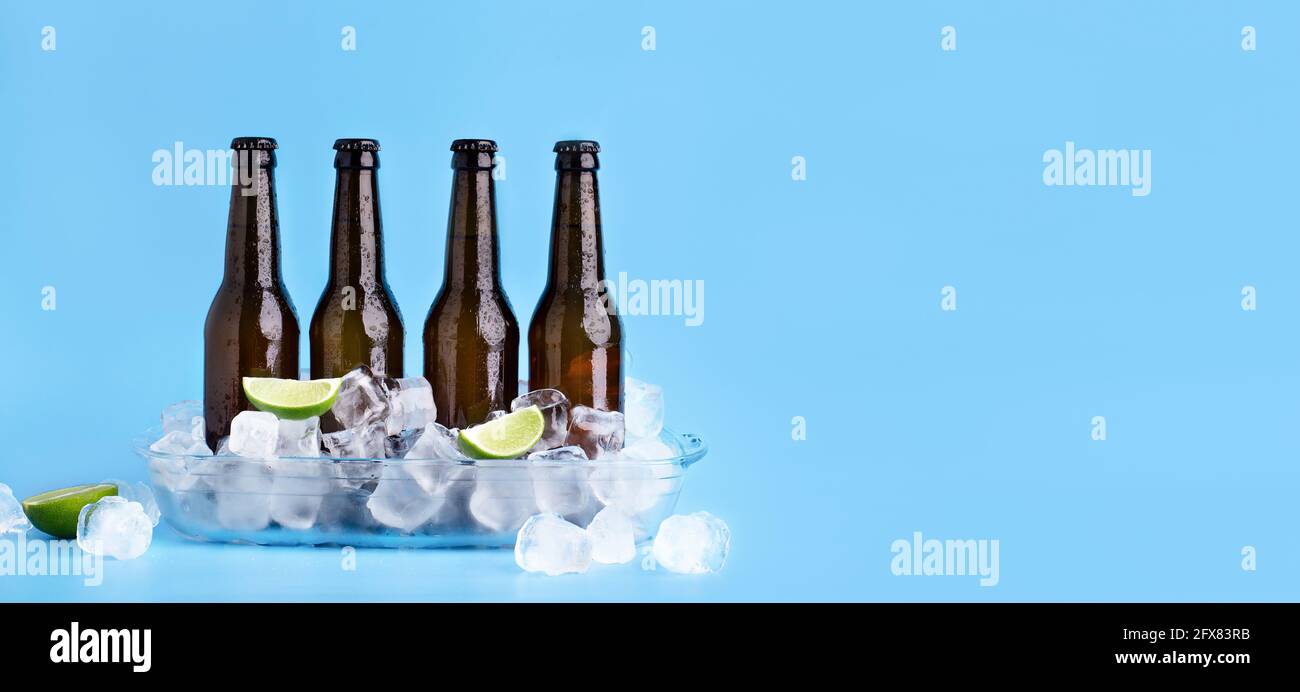 Bottiglie piene di birra scura senza etichette, con cubetti di ghiaccio e con pezzi di lime con gocce fluenti Foto Stock