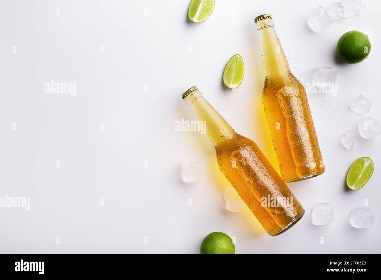 Due bottiglie di vetro completamente trasparenti con ale senza etichette, con gocce fluenti, giacciono con ghiaccio e pezzi di calce Foto Stock