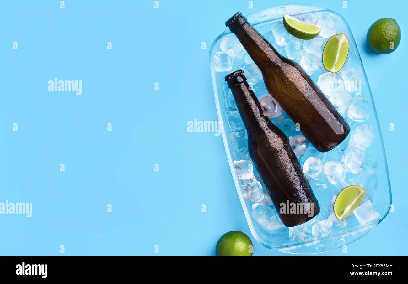 Due bottiglie piene di birra scura senza etichette, si stendono con cubetti di ghiaccio e pezzi di lime con gocce che scorrono Foto Stock
