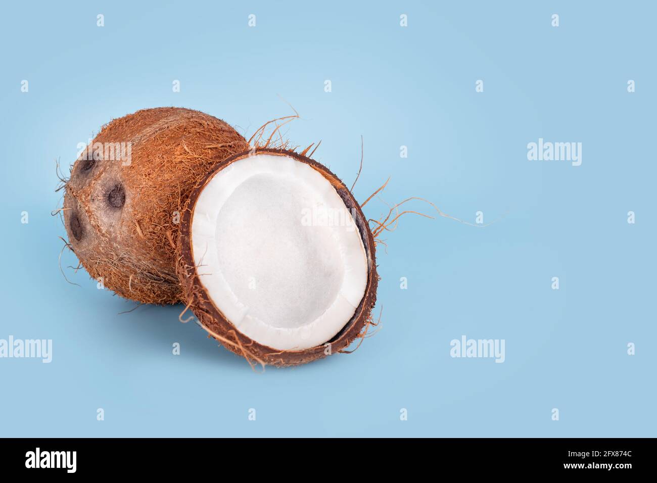 Noci di cocco intere e incrinate su sfondo azzurro. Frutta di cocco sbucciata che mostra i tre pori caratteristici. Tagliare a metà la chiocciola di cocco. Foto Stock