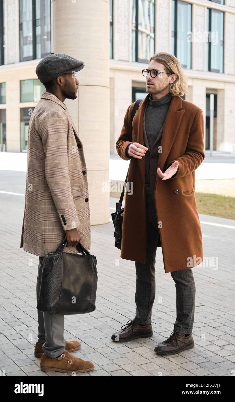 Due colleghi di lavoro in cappotti che discutono qualcosa mentre si levano in piedi all'aperto Foto Stock