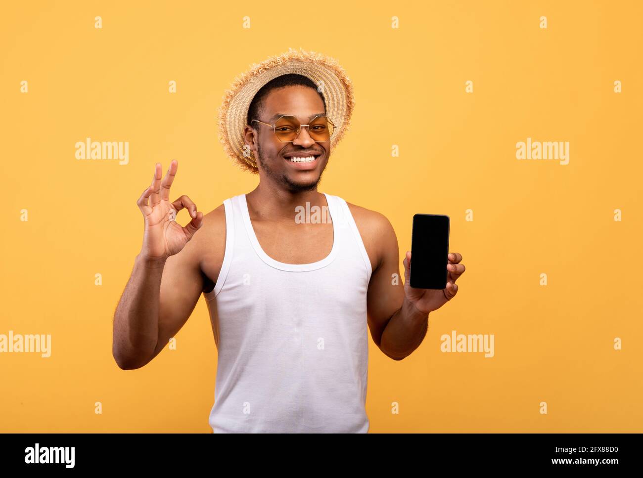 Un ragazzo afro-americano spensierato in estate indossa uno smartphone con mockup, mostrando un gesto corretto Foto Stock