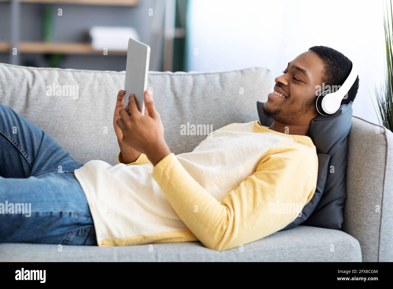 Ragazzo nero sorridente che si stesa sul divano, guardando i film sul pad Foto Stock