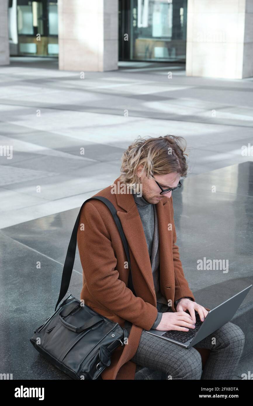 Giovane lavoratore in ufficio in occhiali digitando sul computer portatile e lavorando online in città Foto Stock