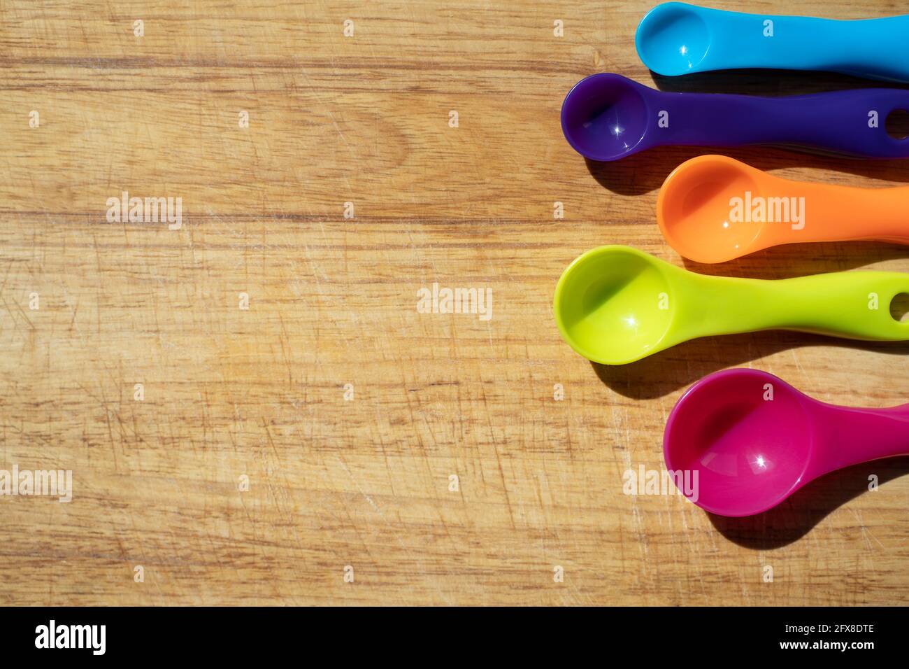 Usato tagliere da cucina in legno con cucchiai di misurazione colorati sul lato. Vista dall'alto del banner Foto Stock