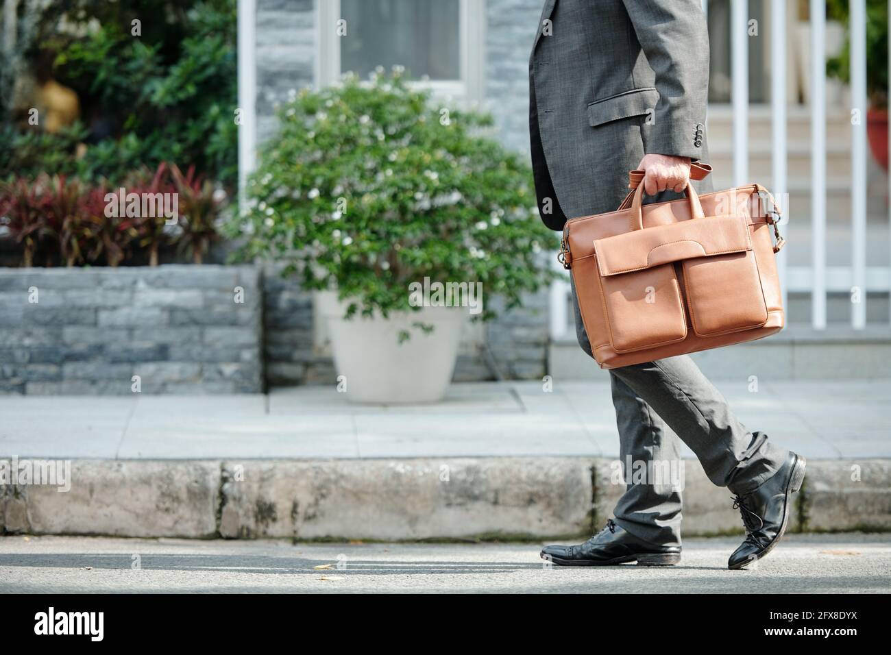 Uomo d'affari irriconoscibile in tuta grigia che trasporta la valigetta mentre cammini via della città Foto Stock