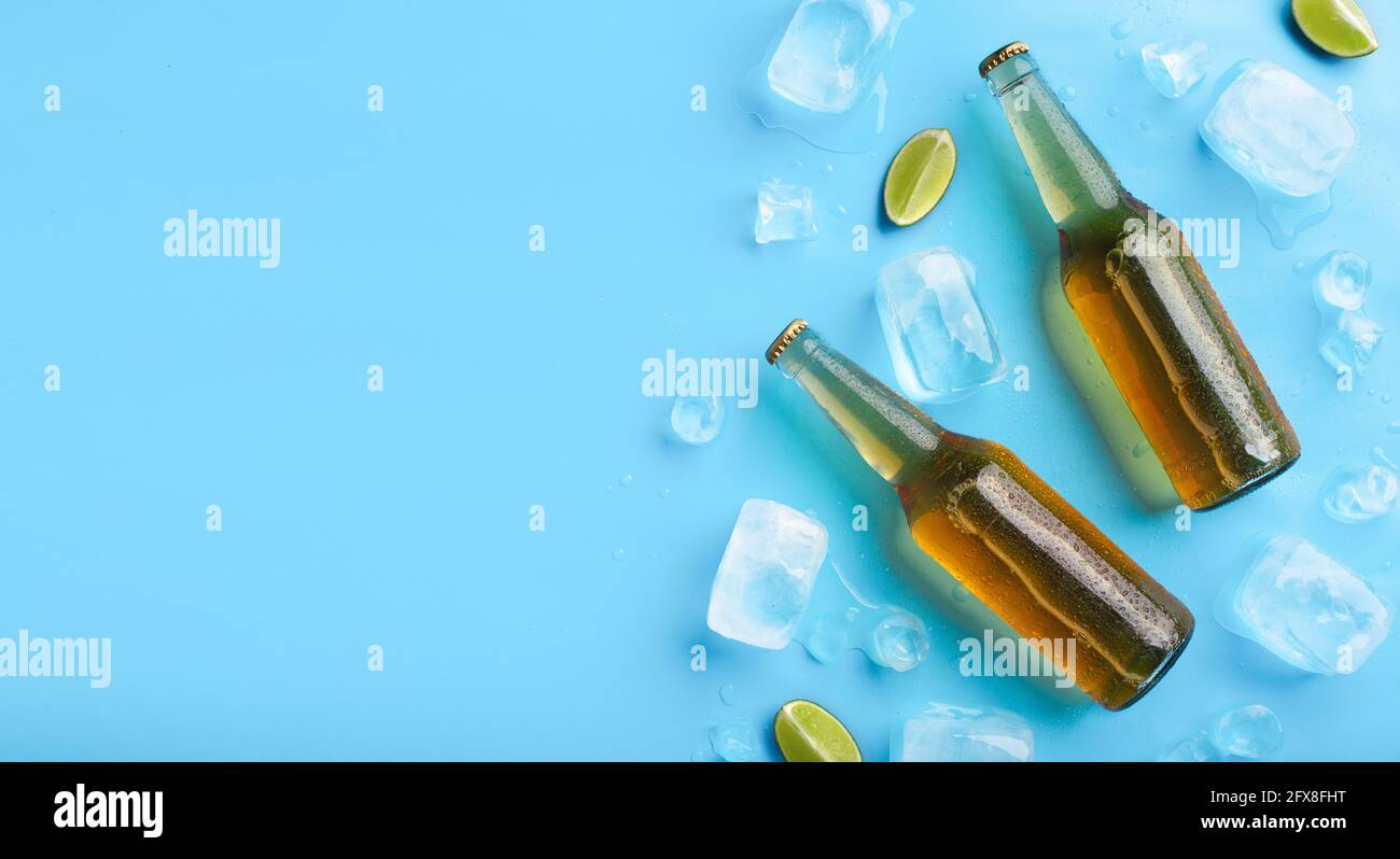 Due bottiglie di vetro piene con lager senza etichette con gocce gocciolanti, giacciono con cubetti di ghiaccio e calce Foto Stock