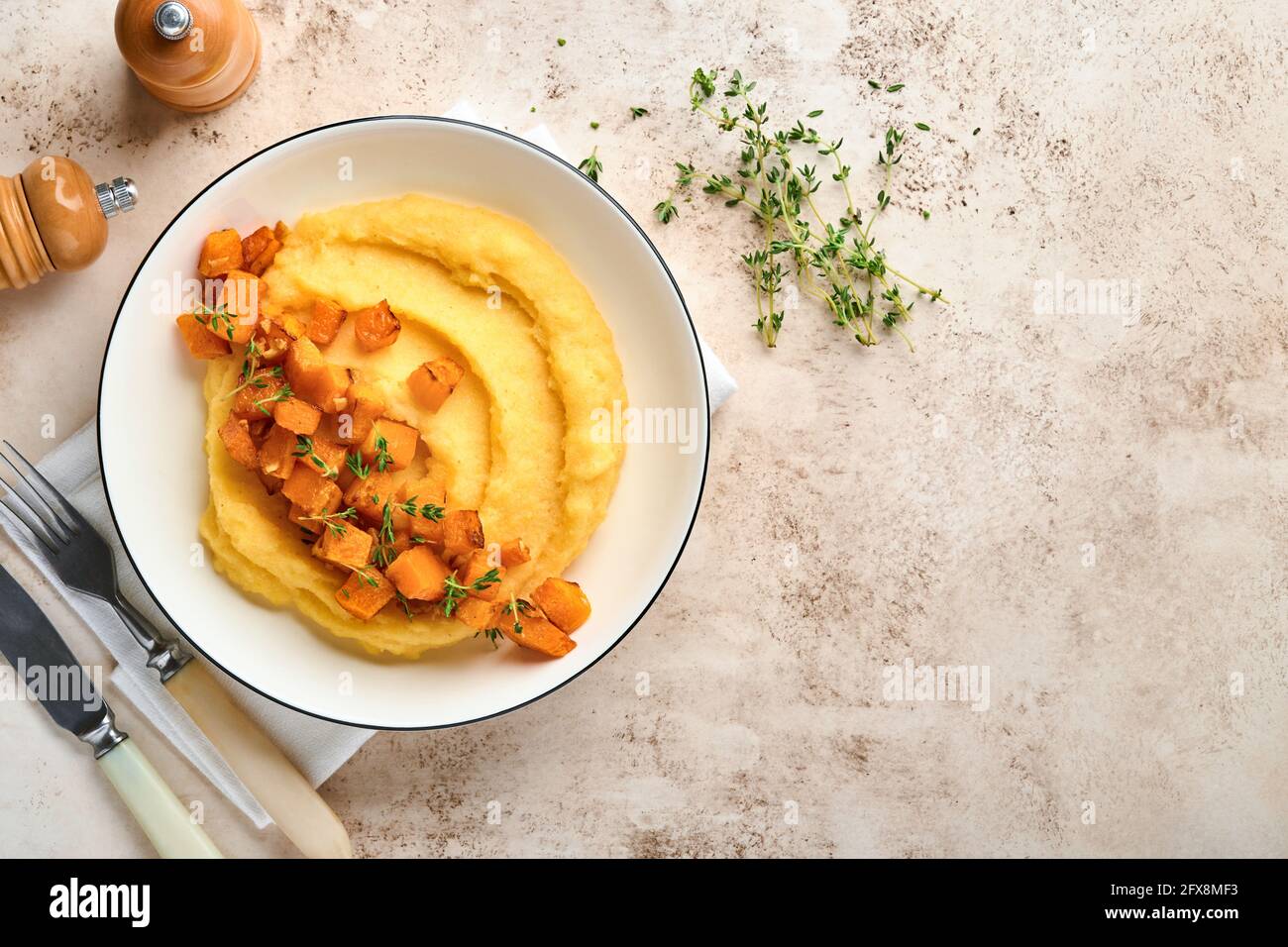 Polenta con burro, zucca, aglio, formaggio salato e parmigiano in ciotola bianca su fondo di cemento chiaro. Cucina tradizionale Italiana di base, vegana Foto Stock