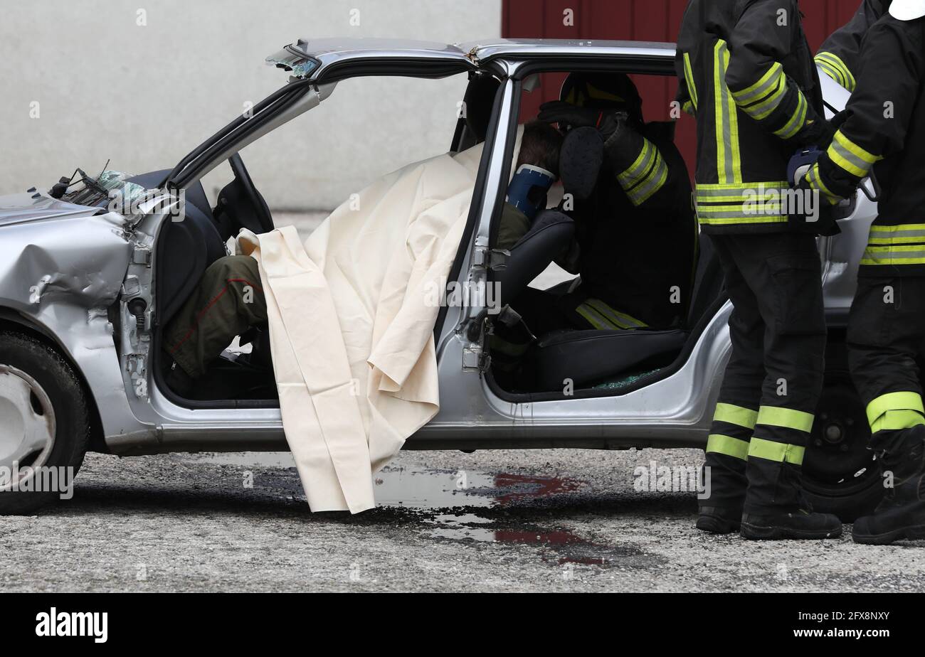 Squadra di Vigili del fuoco durante il salvataggio della persona ferita dopo l'incidente della macchina e l'auto distrutta Foto Stock