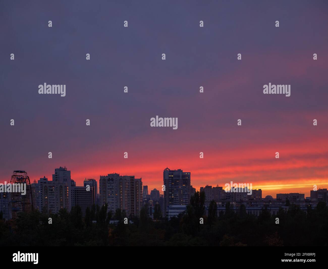 Incredibile tramonto viola, viola, rosso e giallo sulla città di Kiev (Kiev) con edifici, una ruota di osservazione e la chiesa a cupola all'orizzonte. Industriale. Foto Stock