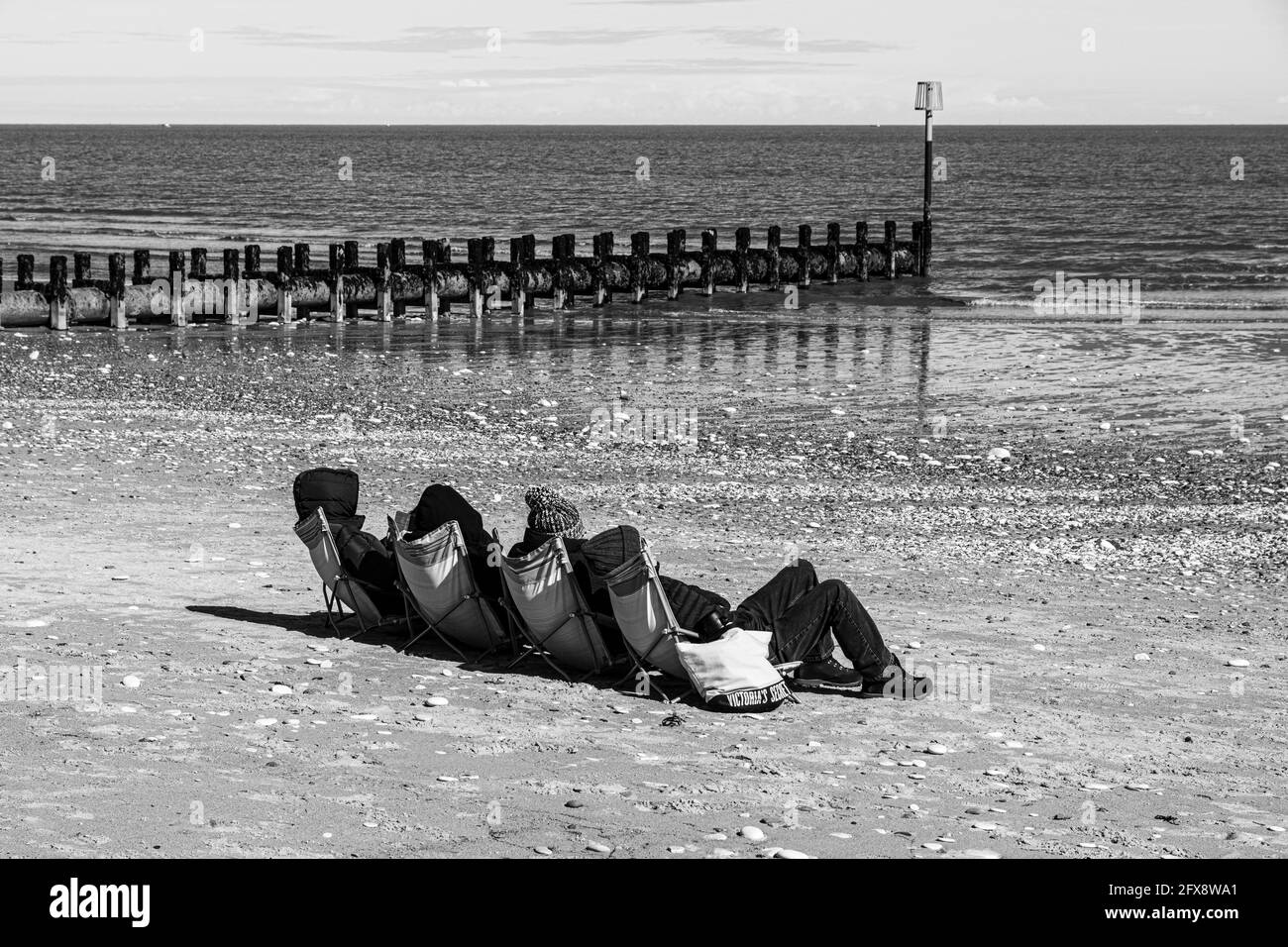 Quattro persone che prendono il sole a metà aprile accanto al Mare del Nord a Bridlington, East Riding of Yorkshire, Inghilterra Regno Unito. Versione a colori 2FX8WD0 Foto Stock