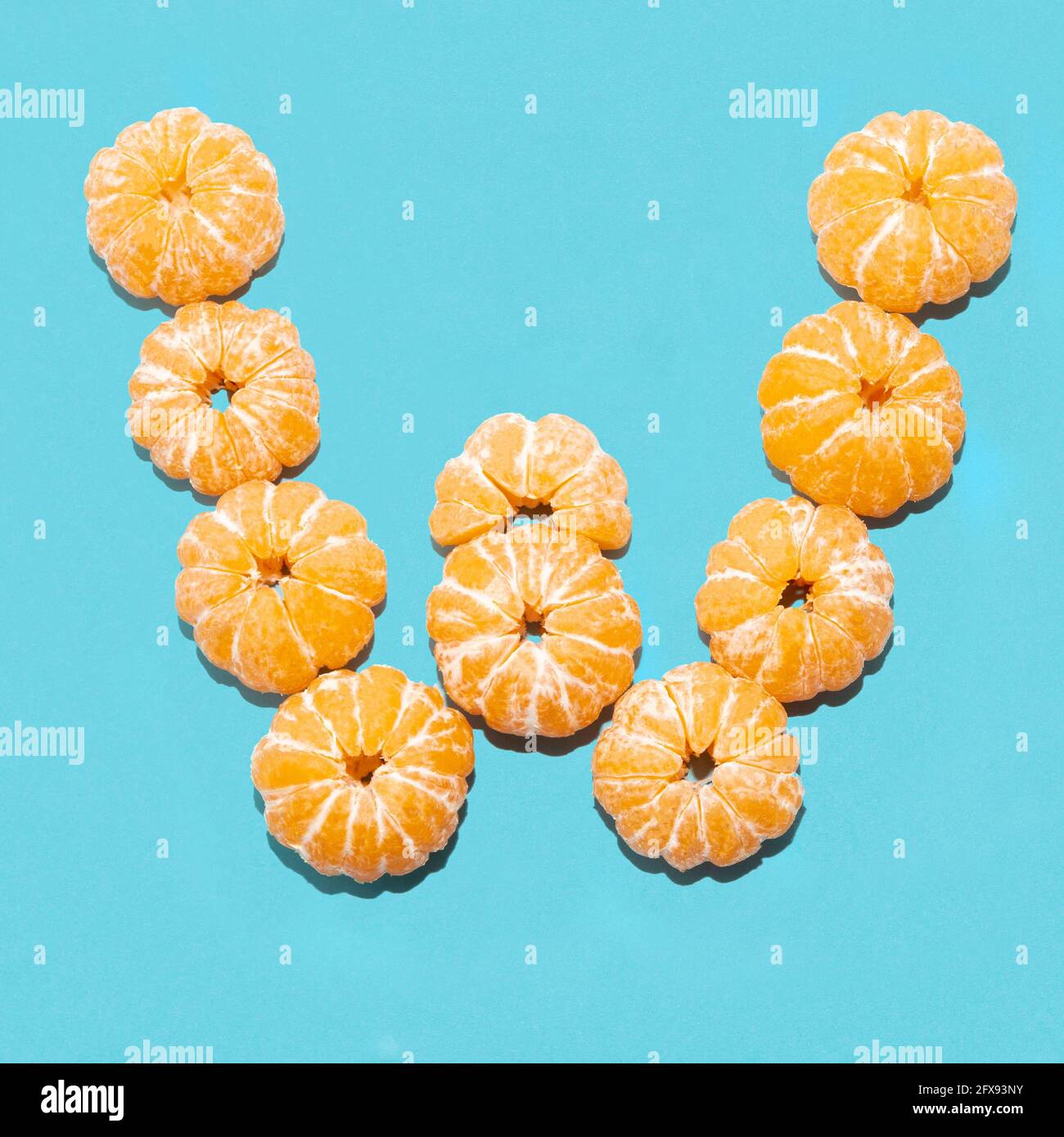 Layout creativo della lettera W da tangerini sbucciati su sfondo blu. Piatto. Foto Stock