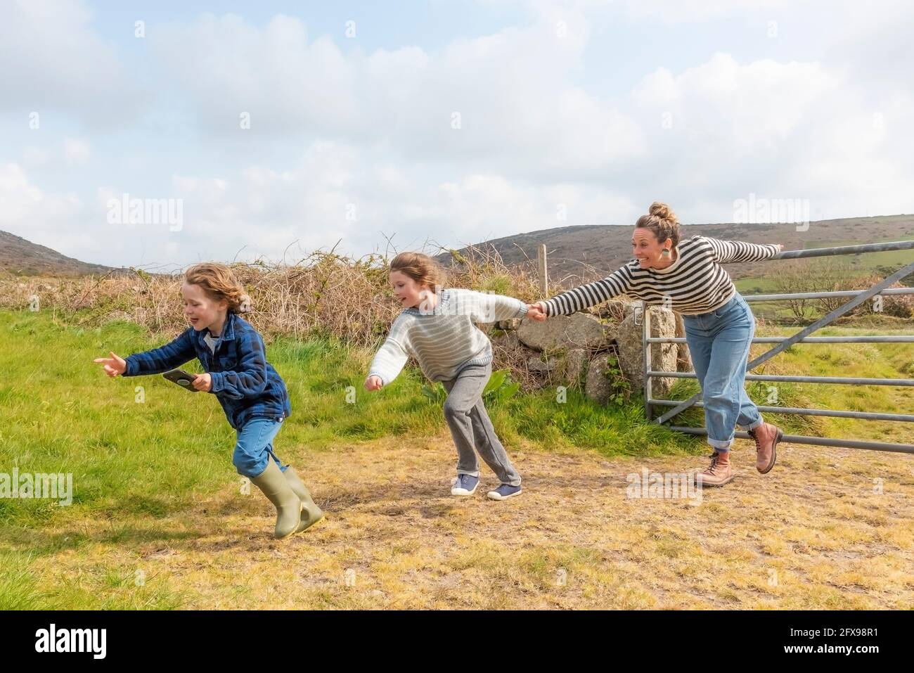 Una madre e i suoi figli si divertono a correre in un campo nella zona di West Penwith in Cornovaglia. Foto Stock