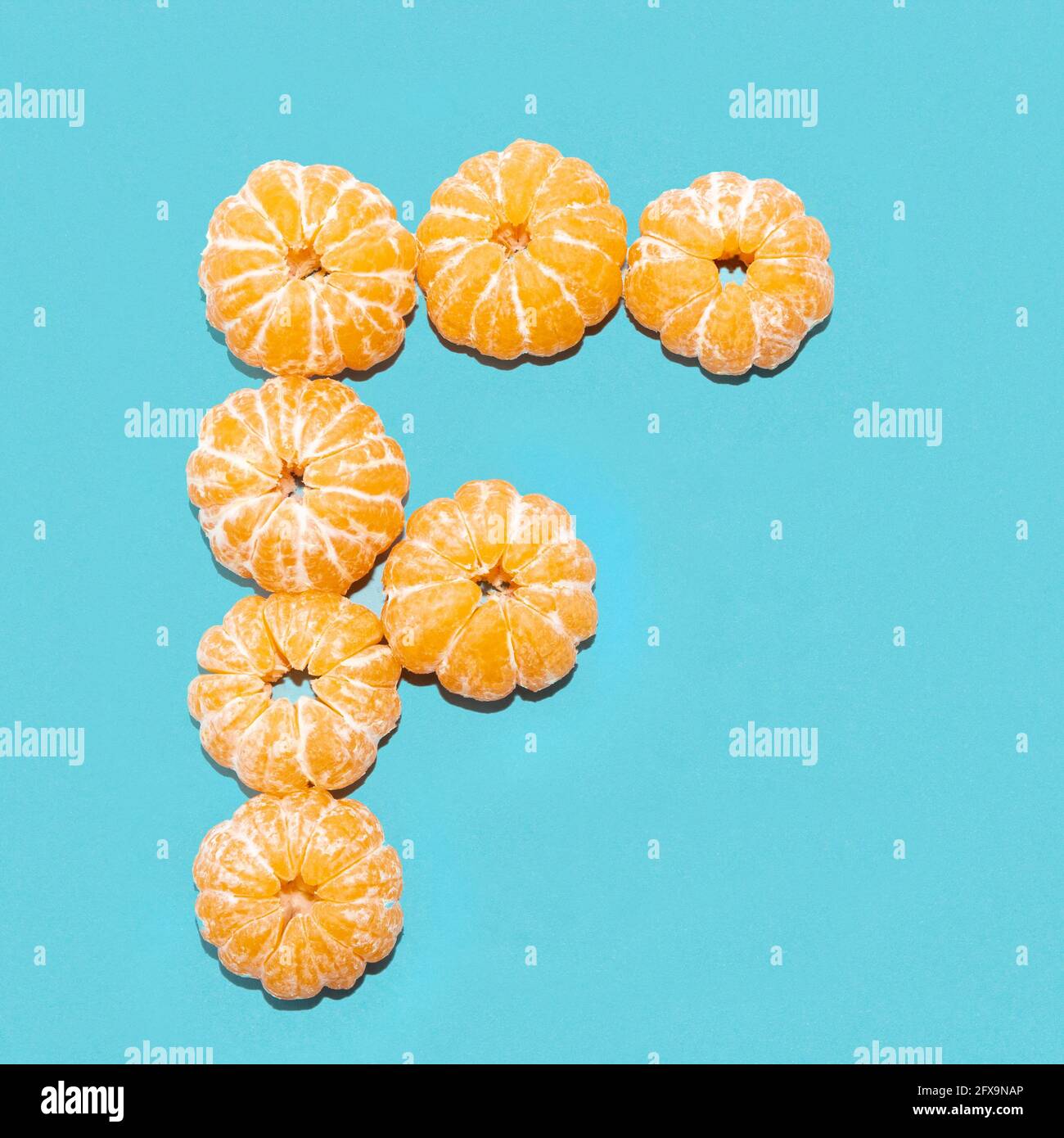 Layout creativo della lettera F da tangerini sbucciati su sfondo blu. Piatto. Foto Stock