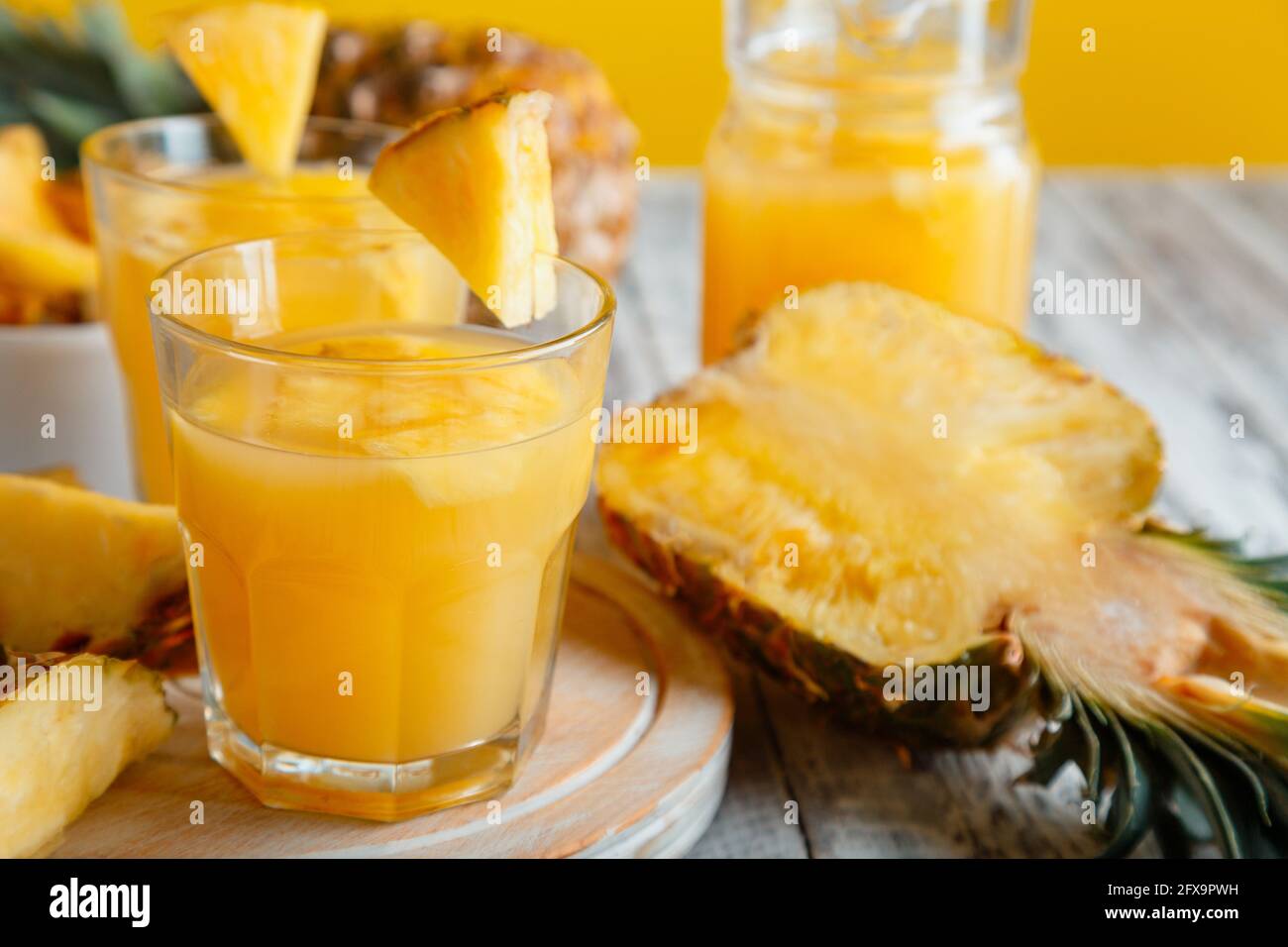 Saporito succo di ananas in bicchiere con fette di frutta all'ananas. Fresco cocktail di ananas naturale e succo in vetro su tavolo di legno bianco. Foto Stock