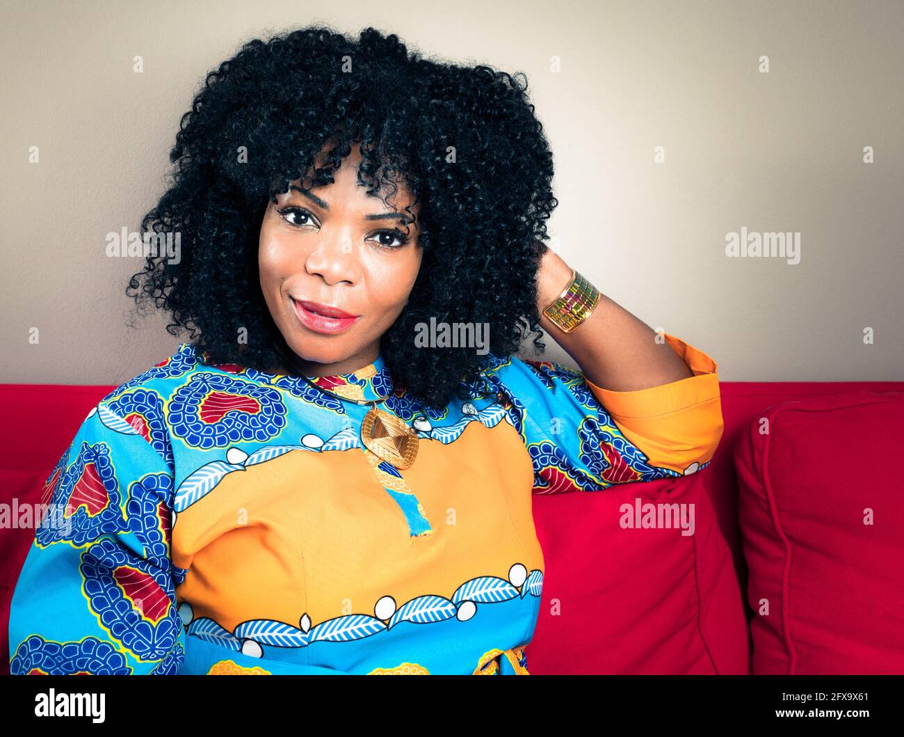 Ritratto orizzontale di una donna afro-americana sorridente seduta un divano rosso Foto Stock