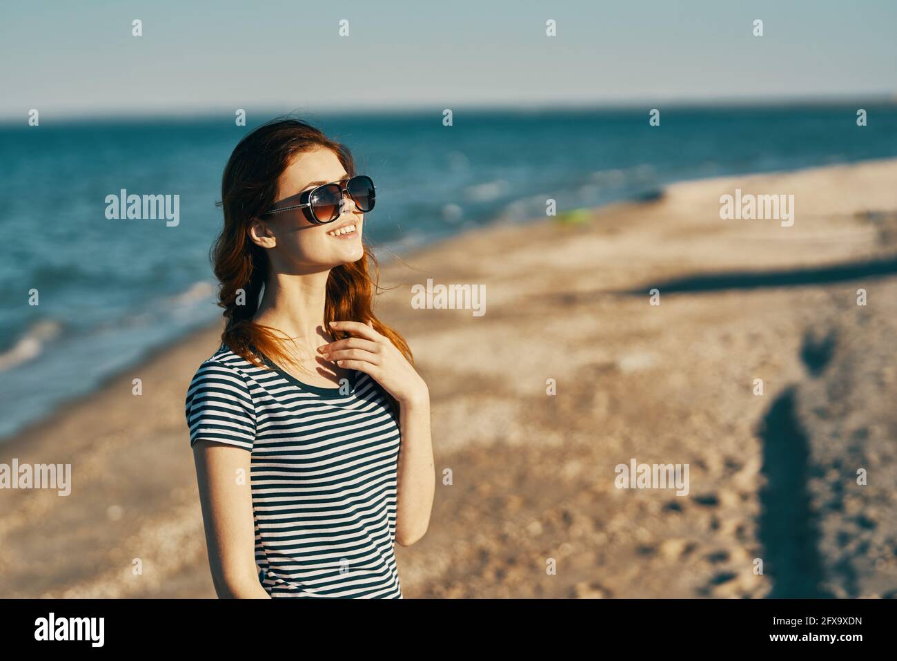 donna dai capelli rossi in occhiali da sole sulla spiaggia vicino al mare  aria fresca vista laterale Foto stock - Alamy