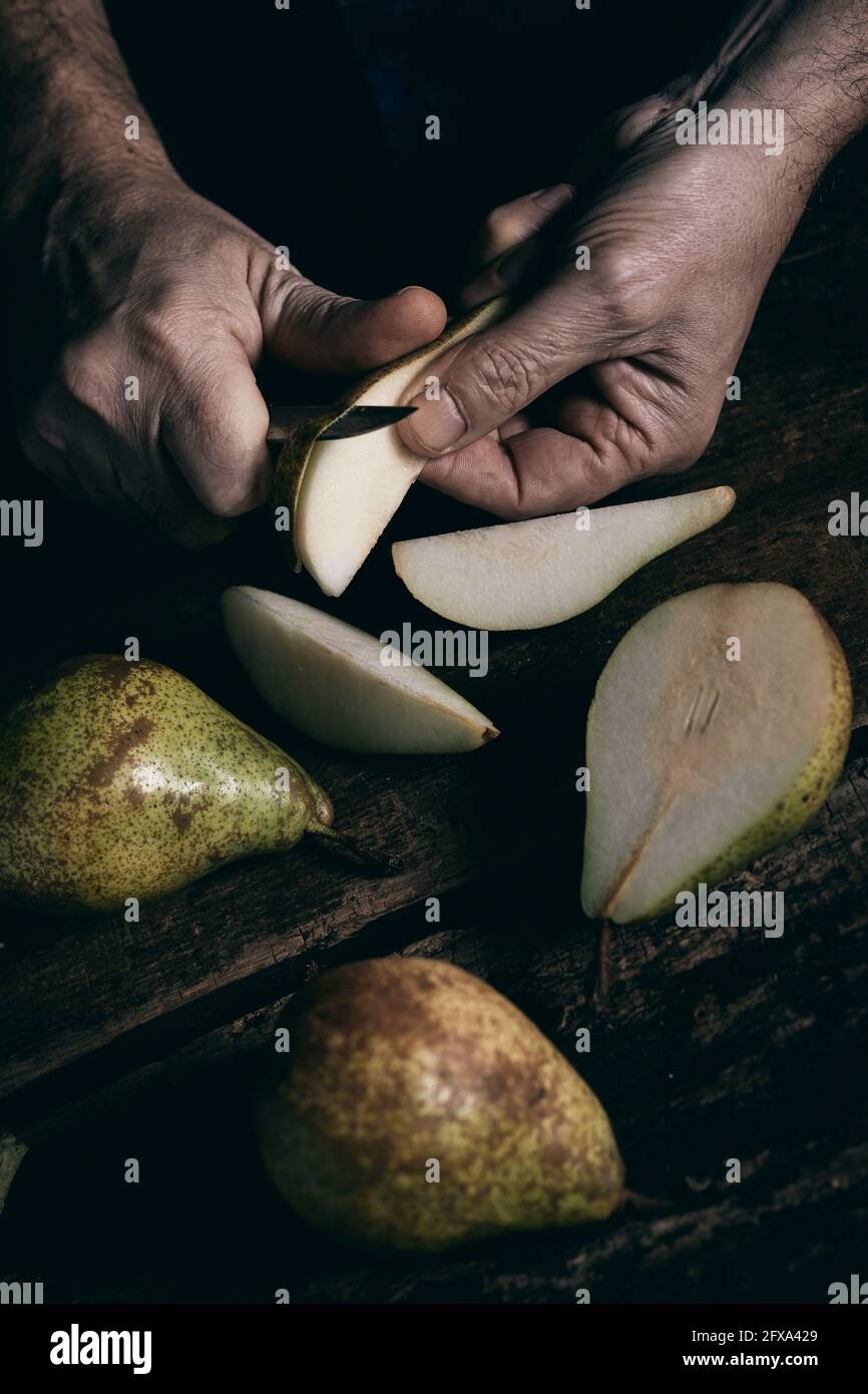 Da sopra l'uomo anonimo peeling pezzi di pere mature sopra tavolo in legno scuro Foto Stock