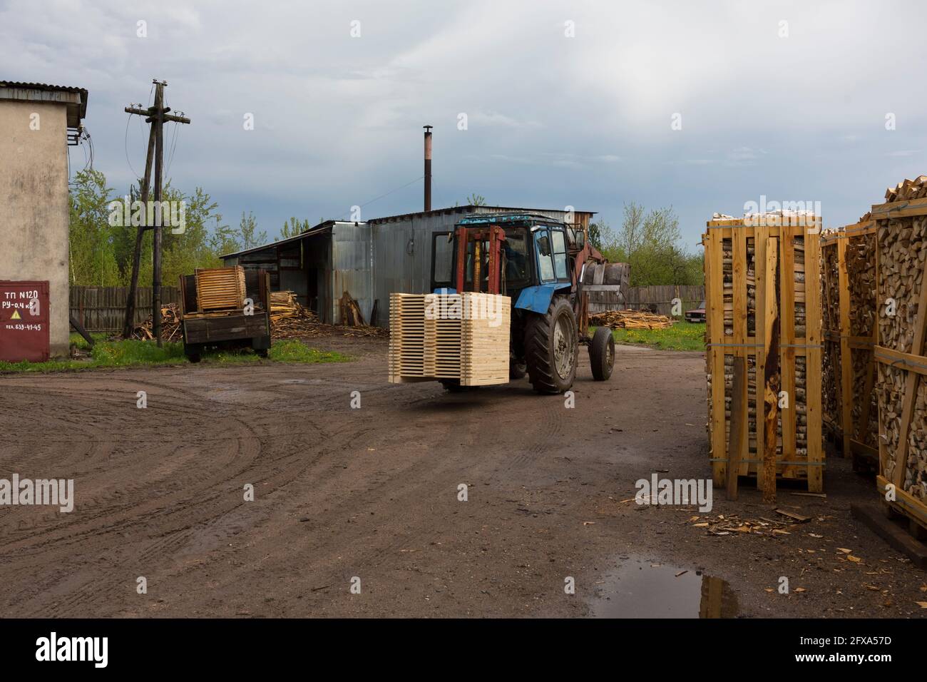 Il trattore carica tavole e legname dal magazzino dei prodotti finiti nel contenitore del carrello Foto Stock