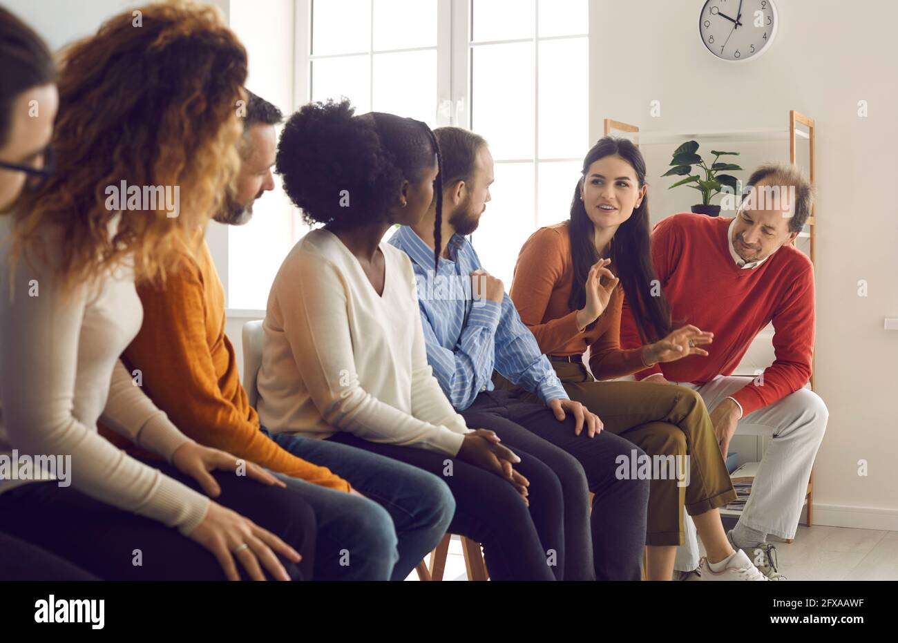 Gruppo di persone diverse che si siedono in fila e ascoltano giovane donna che condivide la sua opinione Foto Stock