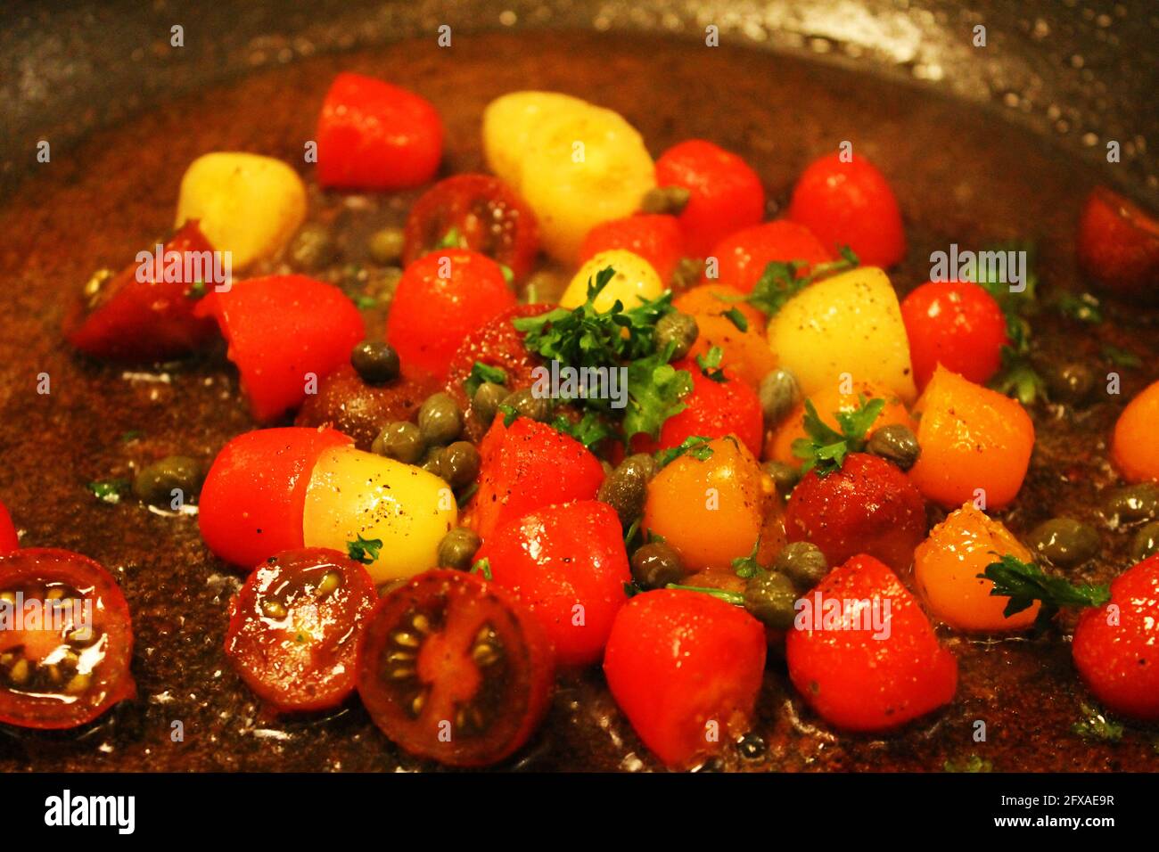 Primo piano di pomodori ciliegini, capperi e coriandolo in una padella friggitrice con olio d'oliva. Foto Stock