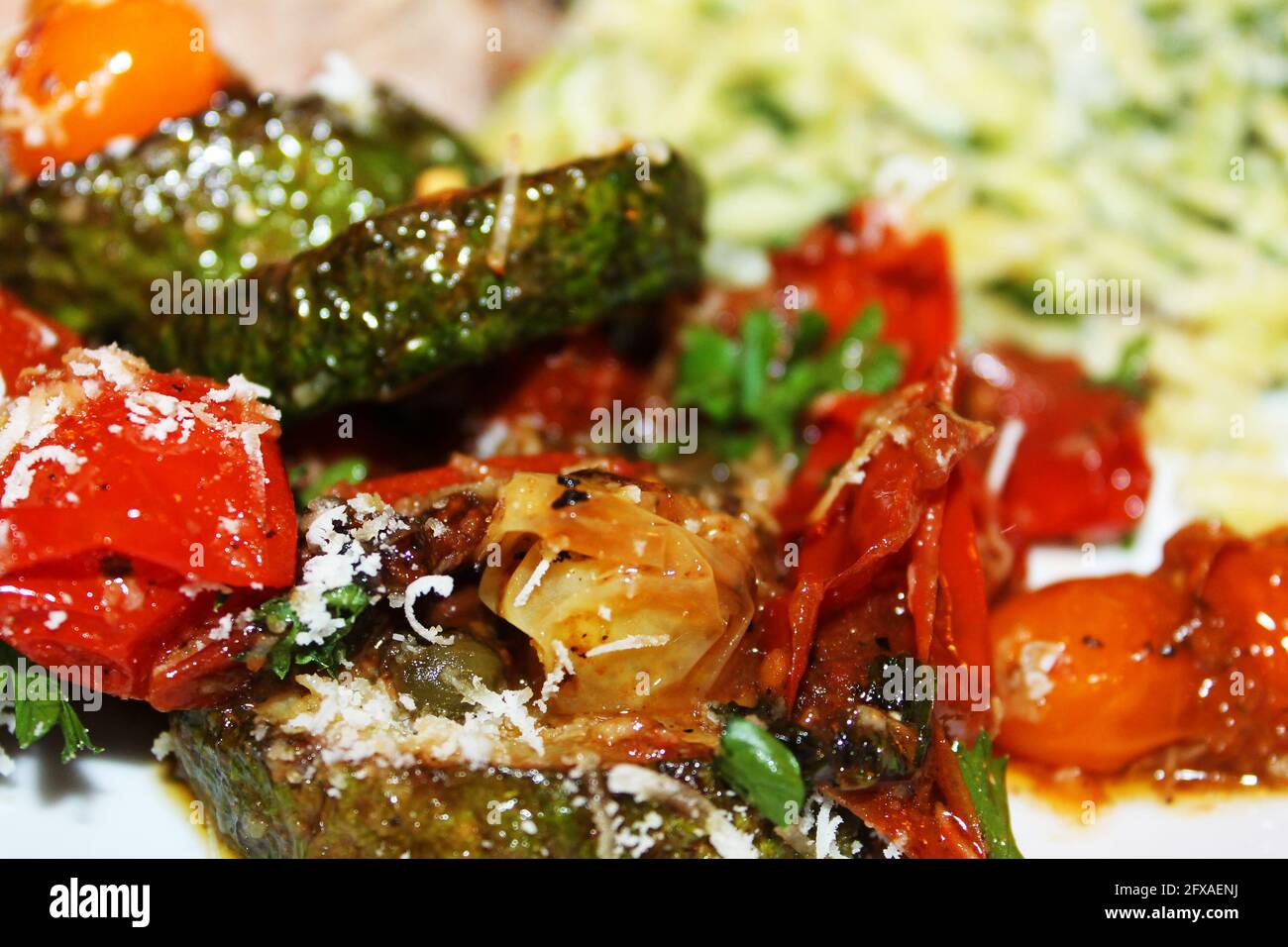 Primo piano di zucchine fritte e pomodori ciliegini, con parmigiano grattugiato, basilico e stagionatura. orzo e bistecca toscana fuori fuoco in background. Foto Stock