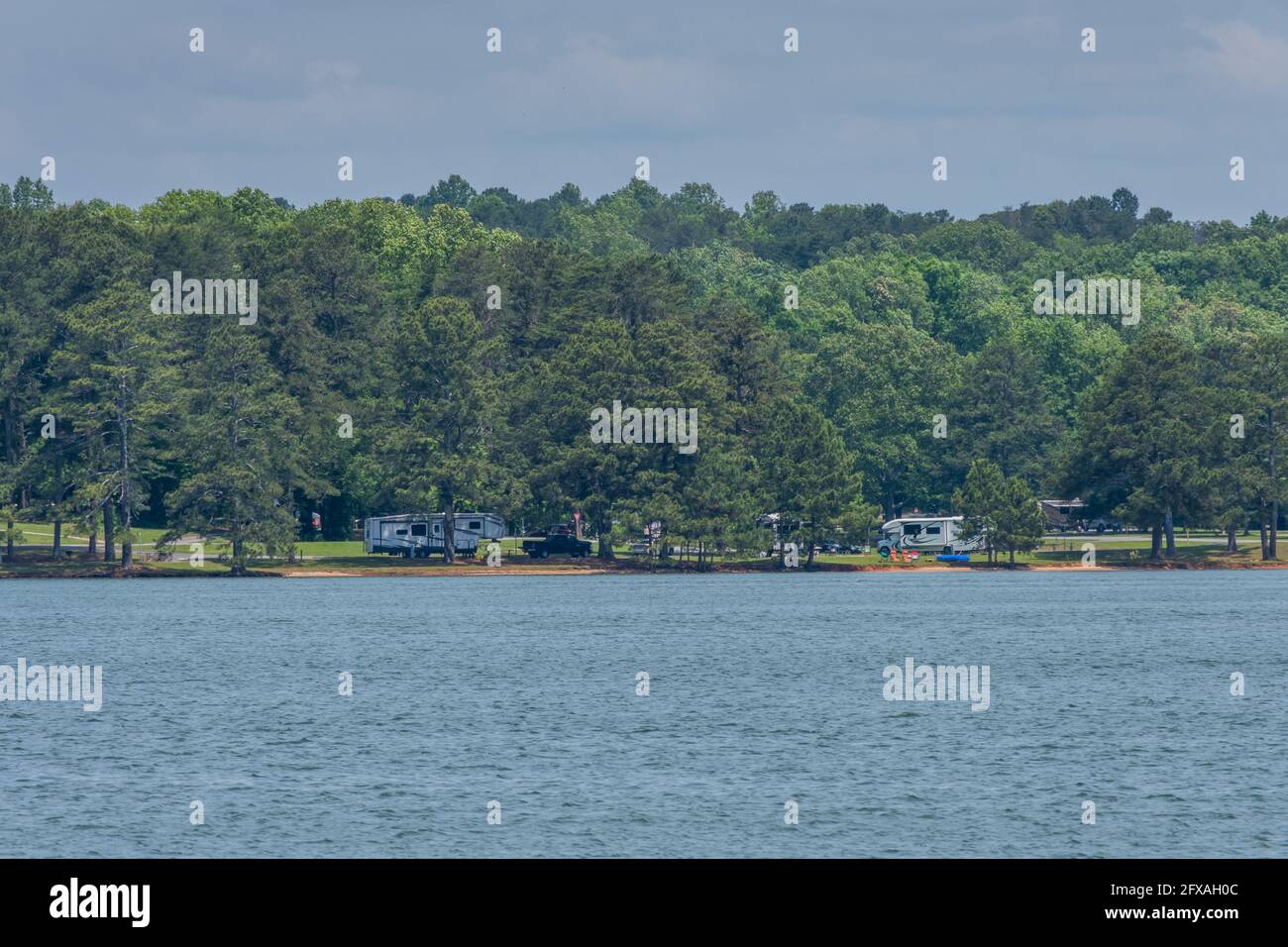Attraverso il lago è un campeggio lungo l'acqua con camper e tende tavoli da picnic e sedie pieghevoli per una vacanza su una calda da umida Foto Stock