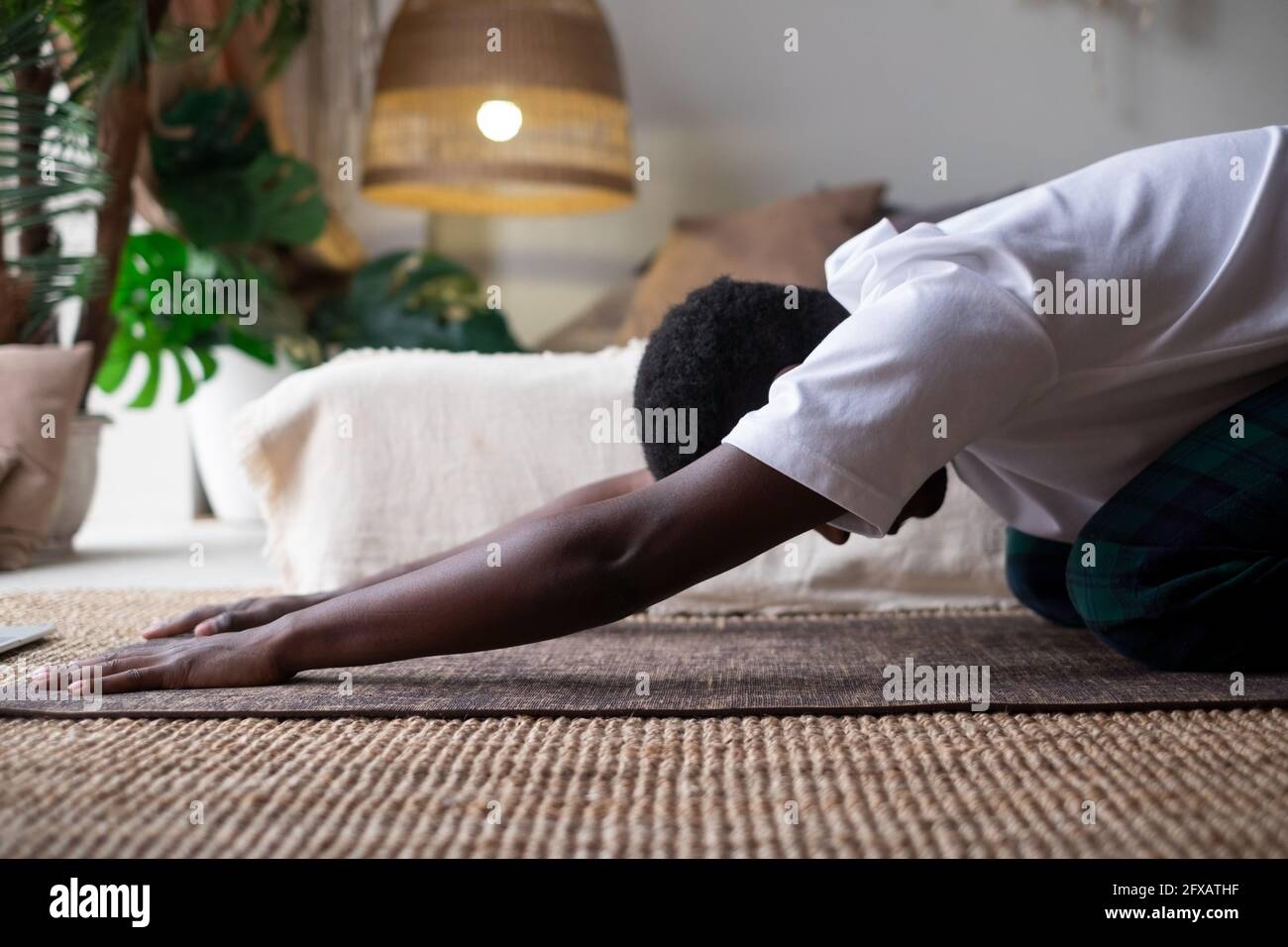 Uomo africano che fa yoga a casa, avendo riposo in balasana o posa bambino, rilassando i muscoli del corpo tra asana Foto Stock