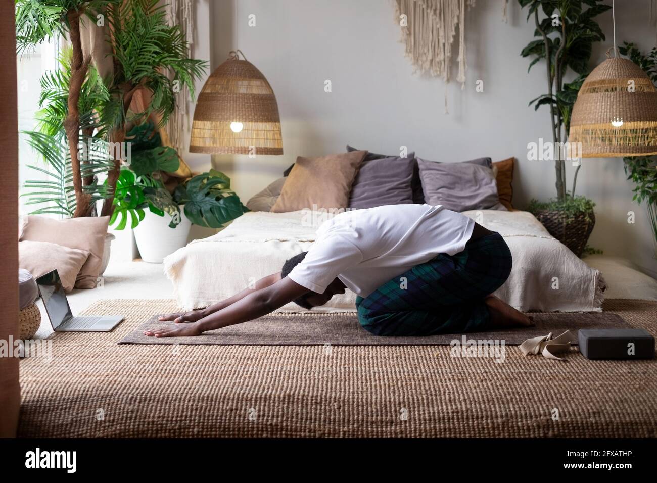 Uomo africano che fa yoga a casa, avendo riposo in balasana o posa bambino, rilassando i muscoli del corpo tra asana Foto Stock