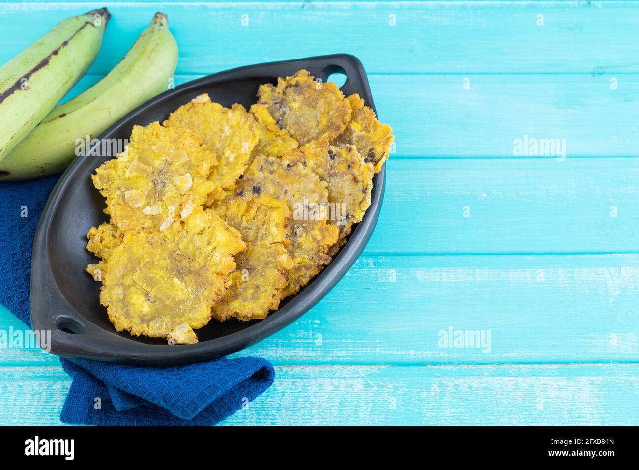 Pataconi fritti in piatto nero su sfondo di legno blu. Spazio di copia. Foto Stock