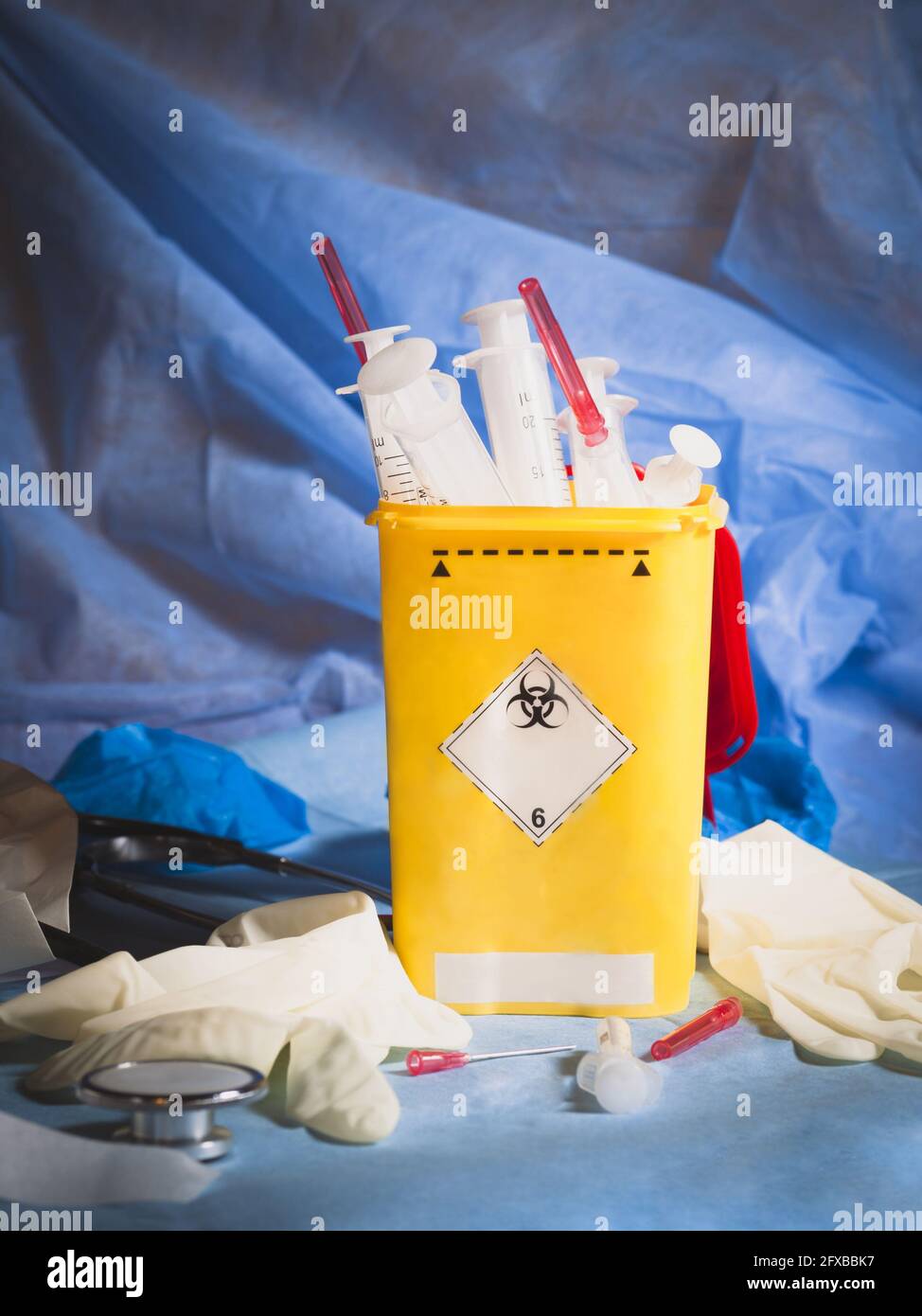 Vista angolata della still life sanitaria con fuoco selettivo verso il contenitore biologico pieno di siringhe e aghi e intorno al materiale clinico: st Foto Stock