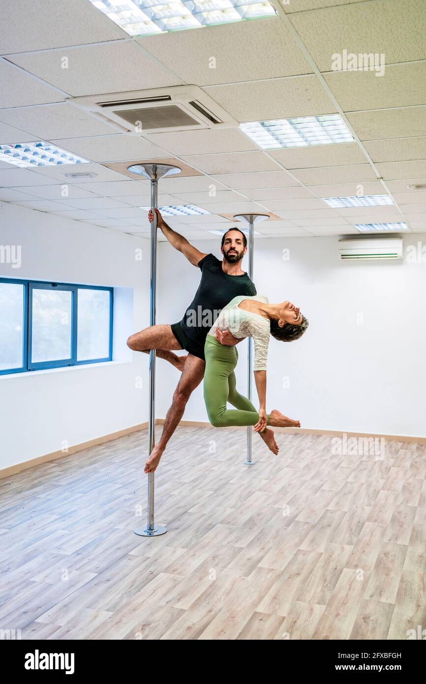 acrobat maschio che porta ballerina femminile mentre appeso su Rod in studio di danza Foto Stock