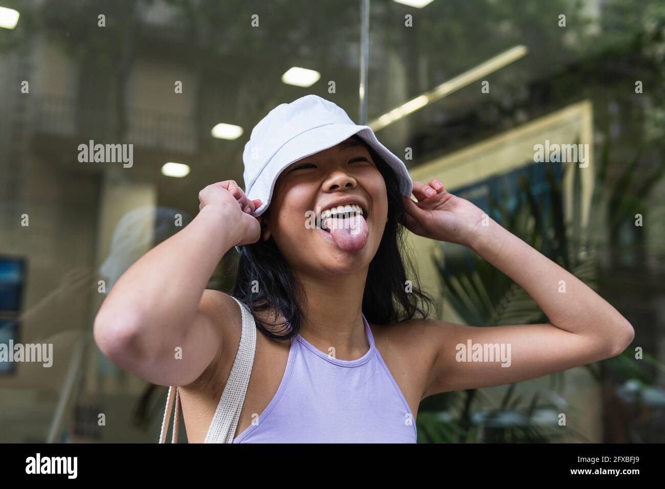 Donna che stacca la lingua mentre tiene il cappello del secchio all'aperto  Foto stock - Alamy