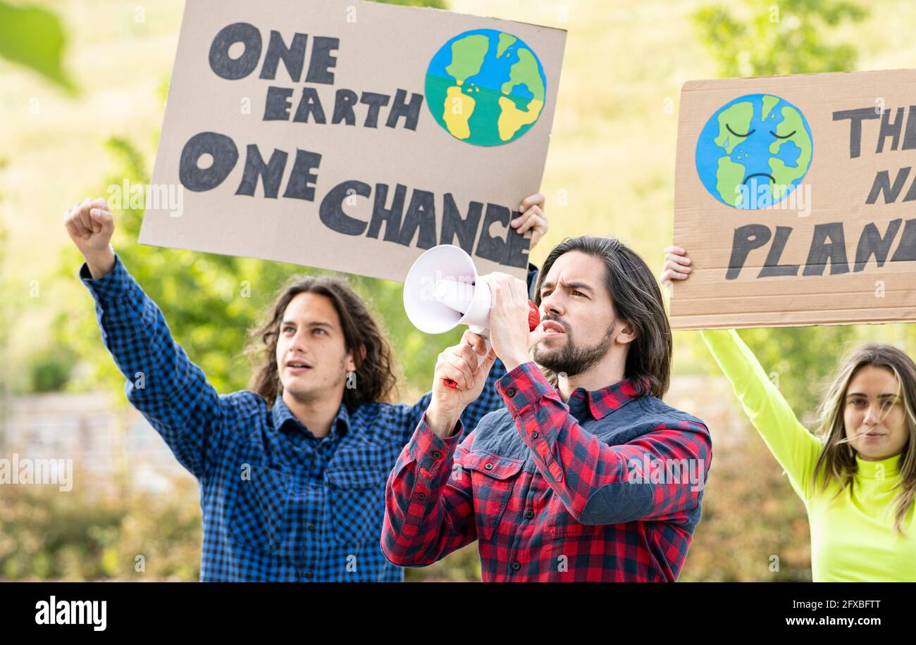 Uomo dai capelli lunghi che tiene un megafono mentre protestava con i manifestanti maschili e femminili contro il cambiamento climatico Foto Stock