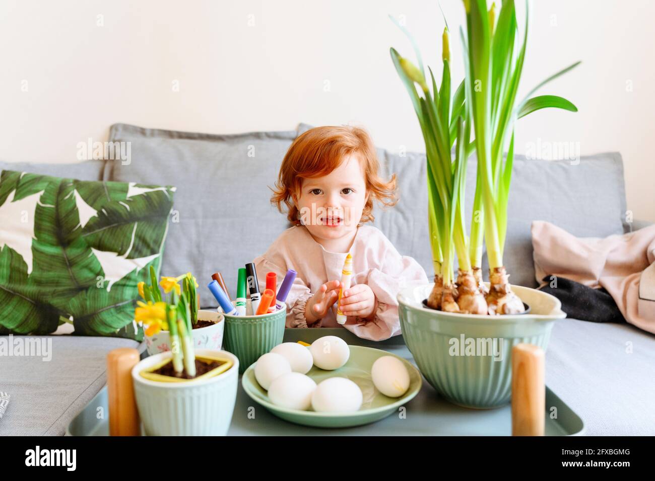 Carino ragazza rossa che tiene la penna della punta del feltro davanti alle uova durante Pasqua a casa Foto Stock