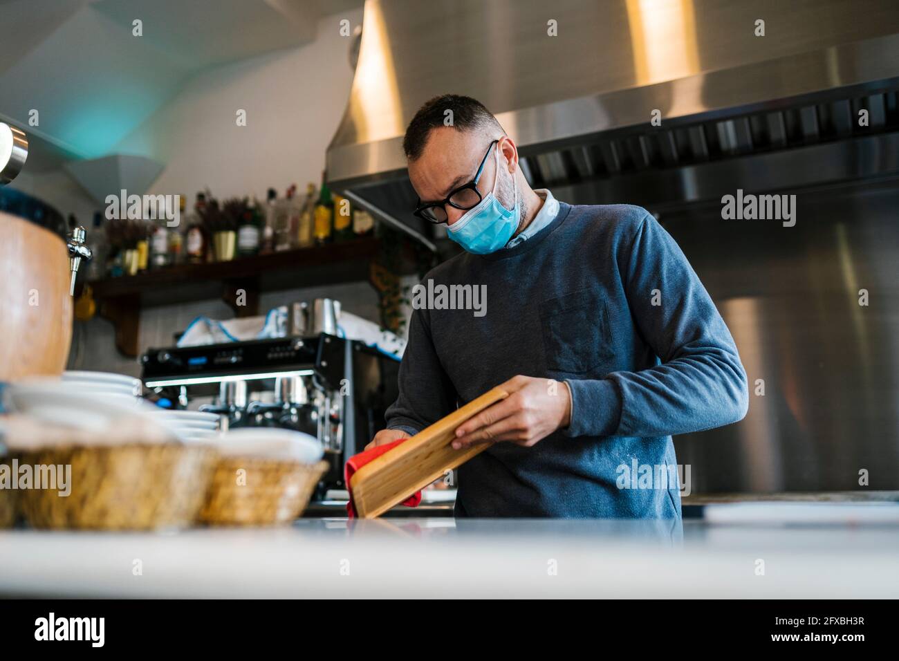 Cameriere con maschera protettiva che strofina il vassoio di legno ad una barra Foto Stock