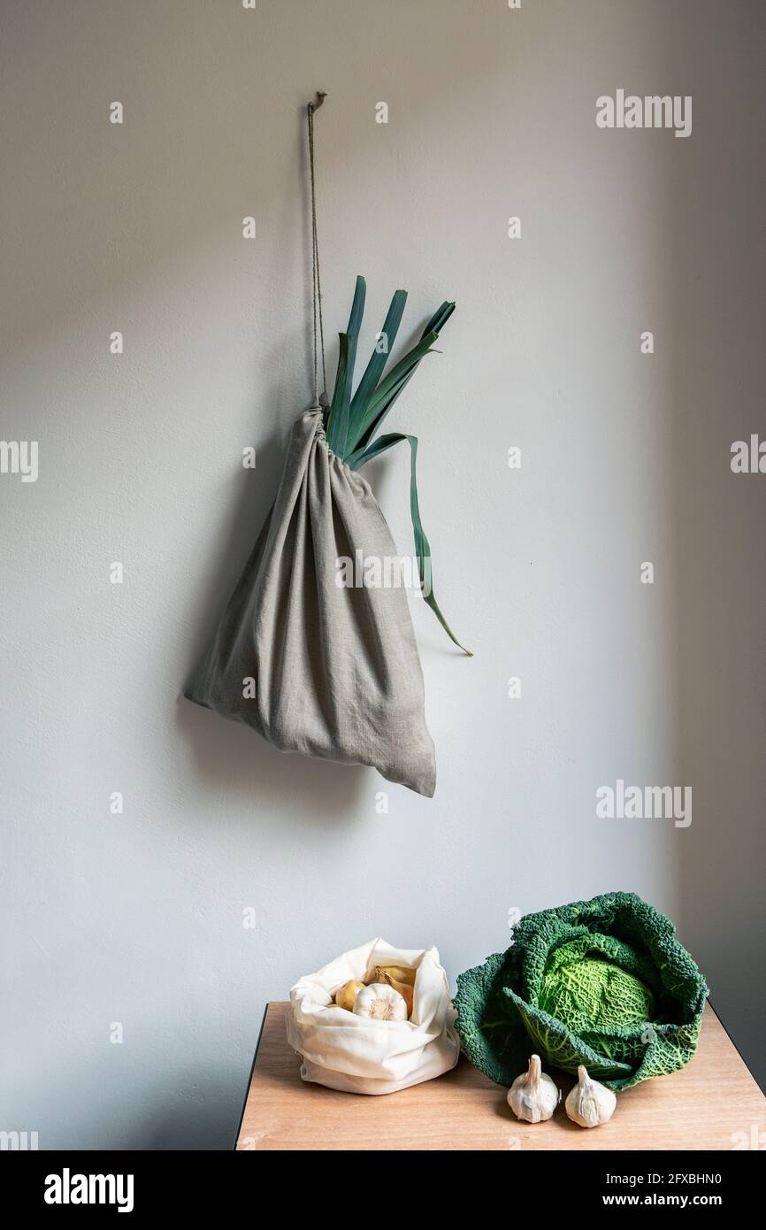 Verdure sul tavolo e borsa di lino appesa su parete bianca Foto Stock