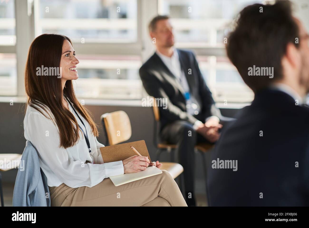 Sorridente imprenditore femminile che partecipa a un evento educativo con i colleghi in ufficio Foto Stock